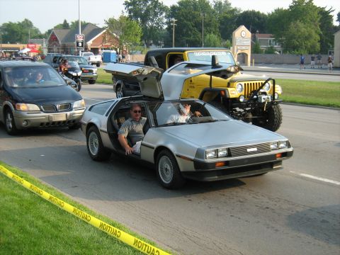 1988 Mercury Grand Marquis - A DeLorean DMC-12 with its iconic doors open is seen driving on a street, accompanied by other vehicles.