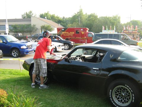 1988 Mercury Grand Marquis - A black 1977 Pontiac Firebird is being cleaned by a person, with other vehicles and an ambulance in the background.