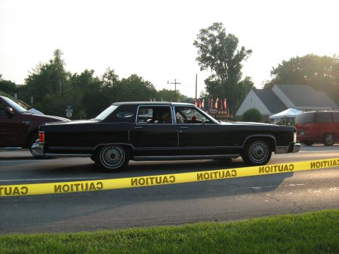1988 Mercury Grand Marquis - A black 1977 Lincoln Continental Mark V sedan is seen from the side, with caution tape across the road.