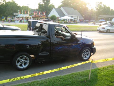 1988 Mercury Grand Marquis - Black pickup truck with custom blue lightning graphics parked near a street event.