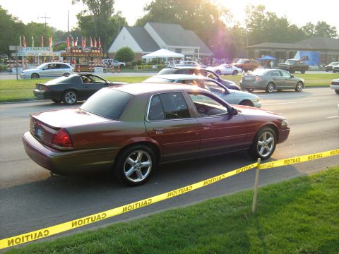 1988 Mercury Grand Marquis - A sedan with a two-tone paint job drives by caution tape at an outdoor event.