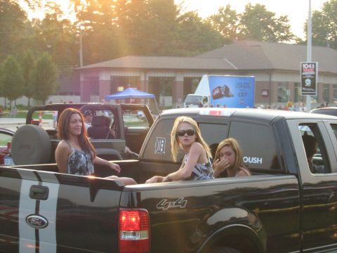 1988 Mercury Grand Marquis - People ride in the back of a pickup truck during a sunny outdoor event.