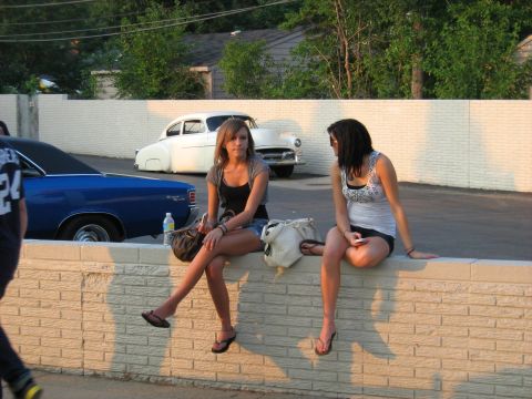 1988 Mercury Grand Marquis - A white classic car from the 1950s is visible in the background behind two women sitting on a wall.