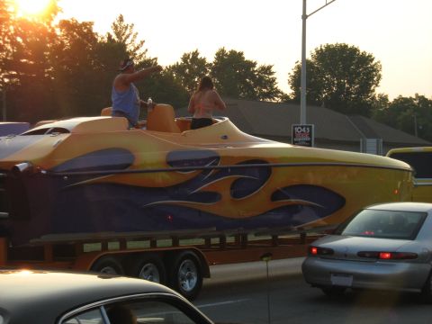 1988 Mercury Grand Marquis - Boat with flame graphics being transported on a trailer, with people onboard. Other vehicles are visible.