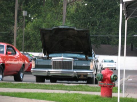 1988 Mercury Grand Marquis - A green sedan with its hood up is parked in front of trees and a building, with a red car to its left.