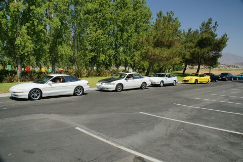 1993 Ford Taurus - A line of cars are parked in a lot, with trees and a distant hill under a clear blue sky.