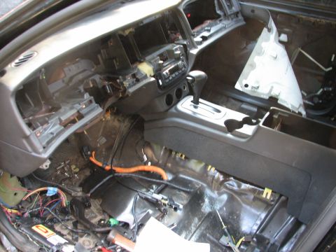 1999 Ford Crown Victoria - Gutted interior of a sedan mid-teardown, shot from the driver's door across a stripped dash with the radio, HVAC controls and column-shift…