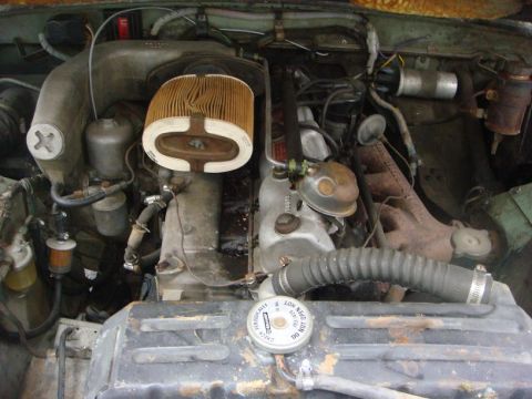 1967 Land Rover Land Rover - Close-up view of the engine compartment, showing various components and hoses. The radiator cap warns against opening when hot.
