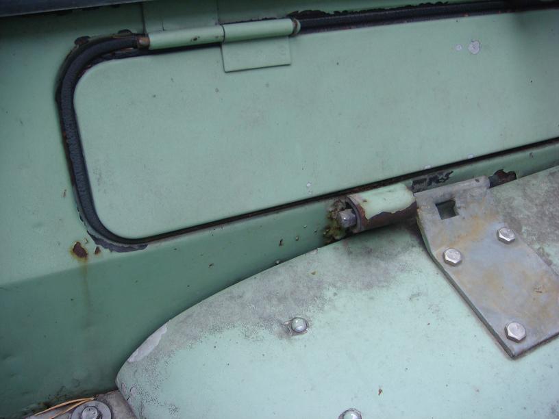 Green vehicle door with visible rust, a hinge, and a metal bracket with bolts