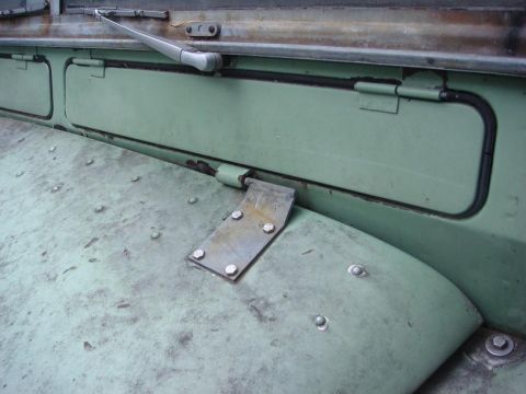 1967 Land Rover Land Rover - Close-up view of the fender and door panel of a green Land Rover, showing rivets and a metal bracket. A windshield wiper is also visible.