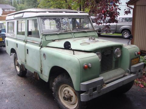 1967 Land Rover Land Rover - A light green 1967 Land Rover Land Rover with a white roof is parked on a wet asphalt surface.