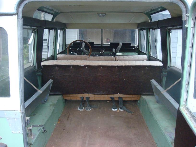 Green 1967 Land Rover Land Rover interior, showing bench seats, wooden floor, and steering wheel