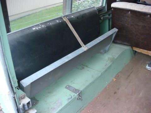 1967 Land Rover Land Rover - Interior view of a vehicle, highlighting the green bench seat and a brown upholstered seat, with a metal bar in the foreground.