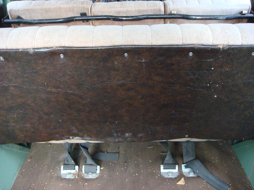 Vehicle interior showing brown faux leather paneling and beige seats with black seatbelts on the floor