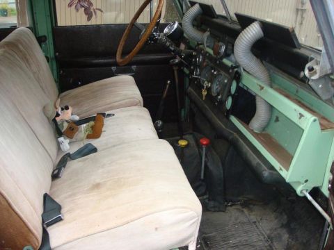 1967 Land Rover Land Rover - The interior of a 1967 Land Rover Land Rover shows tan bench seats, a wooden steering wheel, and distinctive grey vent hoses.