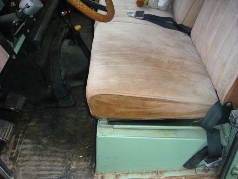 1967 Land Rover Land Rover - Interior view shows tan seats, a green storage box under the passenger seat, and a black seatbelt.