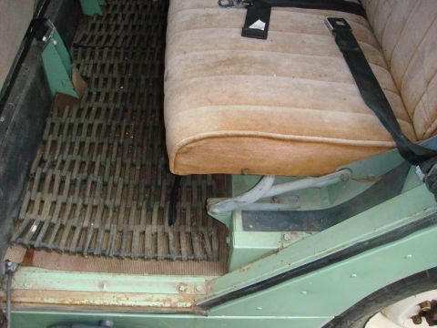 1967 Land Rover Land Rover - Interior view of a vehicle showing a woven floor mat and a tan seat with seatbelts.