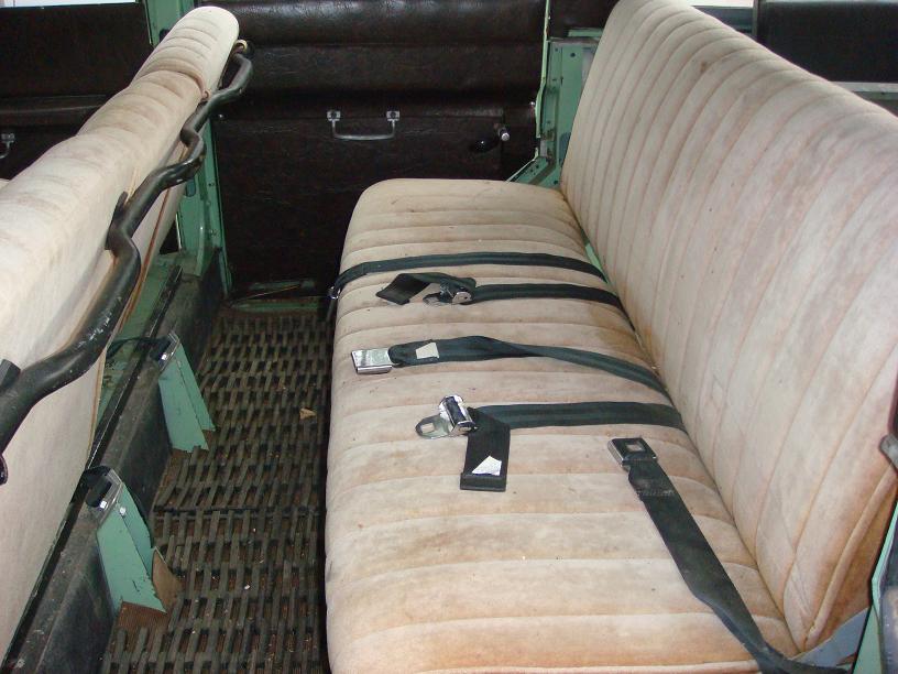 Interior view of a vehicle showing two rows of bench seats with seatbelts and a metal floor mat