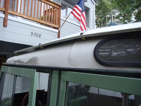 1967 Land Rover Land Rover - The side of a green Land Rover Defender is visible, with a silver roof and an oval window. An American flag flies above.