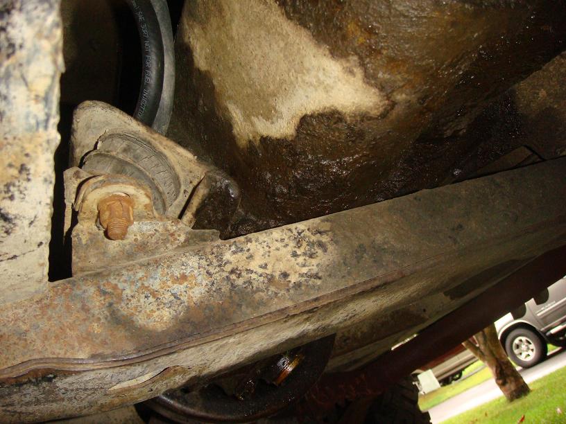 Close-up of rusty underbody components and a black hose, with a glimpse of a van in the background