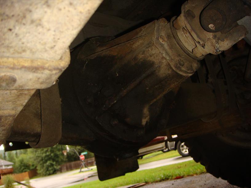 Underside view of a vehicle's driveshaft and differential housing, with some rust visible