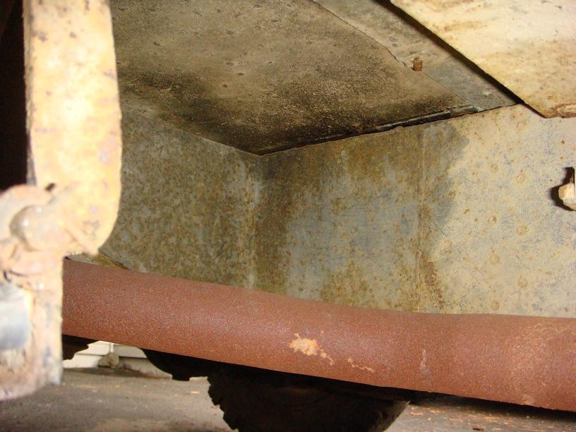 Undercarriage of a rusty vehicle with a large exhaust pipe and visible suspension components
