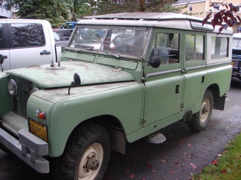 1967 Land Rover Land Rover - A 1967 Land Rover Land Rover is parked on a wet asphalt driveway next to a modern pickup truck.