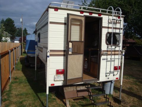 1988 Ford F-350 - This slide-in truck camper is parked in a grassy yard, with a ladder attached to the rear and a license plate visible.