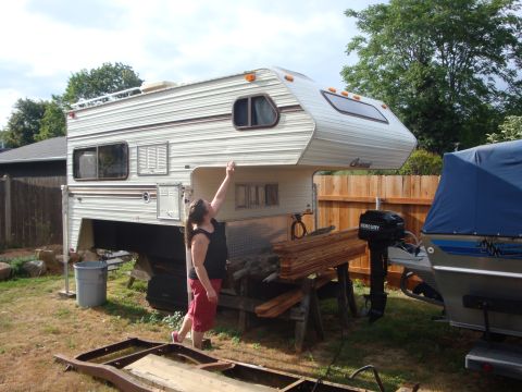 1988 Ford F-350 - A person inspects a truck camper unit in a yard, with a boat and motor nearby.
