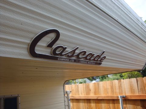 1988 Ford F-350 - The side of a Cascade camper with its logo visible, next to a wooden fence.
