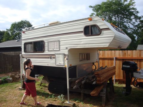 1988 Ford F-350 - A slide-in camper is parked in a yard, with a woman standing nearby and lumber stacked beside it.