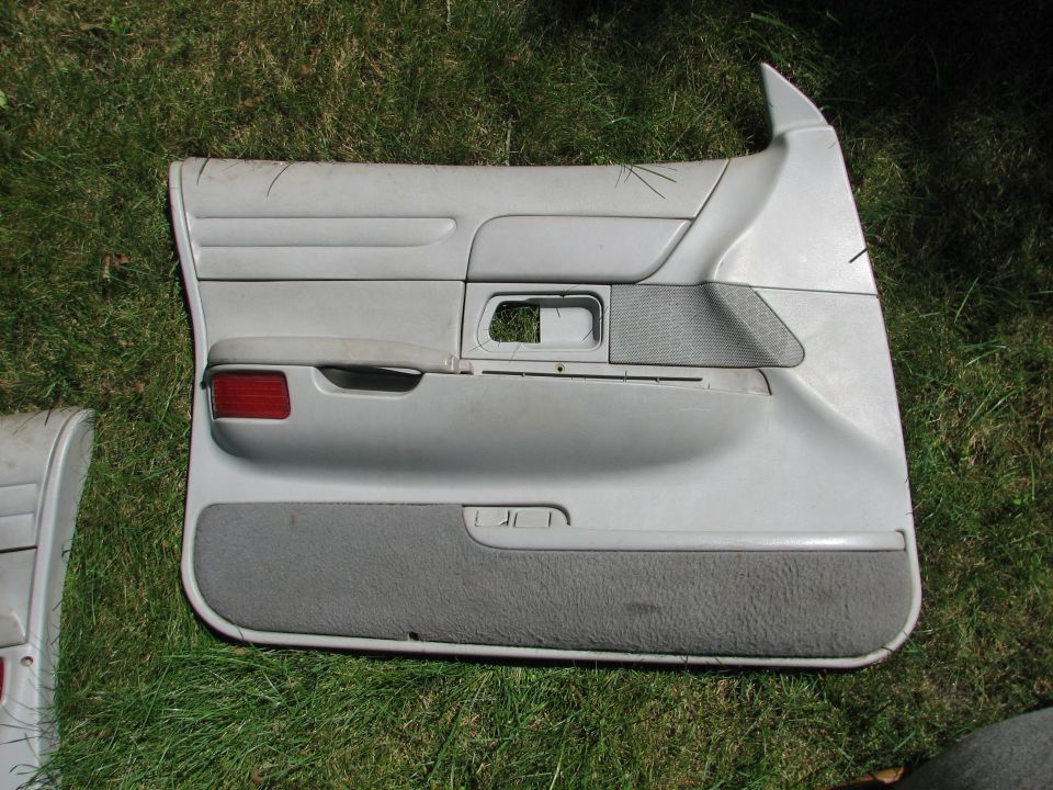 Gray car door panel with red reflector and textured gray armrest, lying on grass