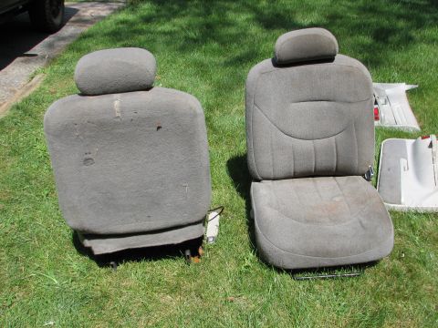 1999 Ford Crown Victoria - Two grey fabric car seats with headrests are displayed on the grass, with one seat showing signs of wear and tear.