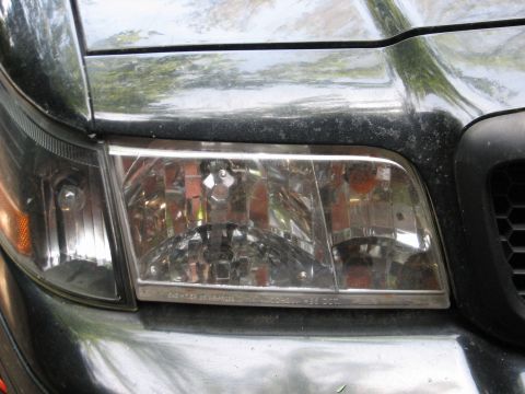 1999 Ford Crown Victoria - Close-up of the front headlight assembly on a black vehicle, showing the clear lens and internal reflectors.