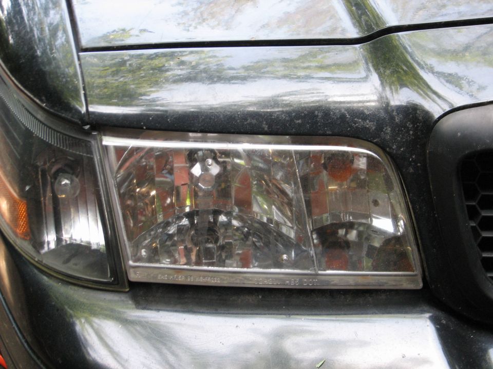 Front headlight assembly of a black car, possibly a 1998 model