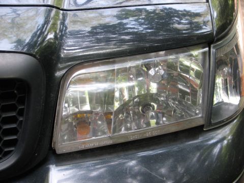 1999 Ford Crown Victoria - Front headlight assembly of a dark-colored vehicle, with visible text on the lens.