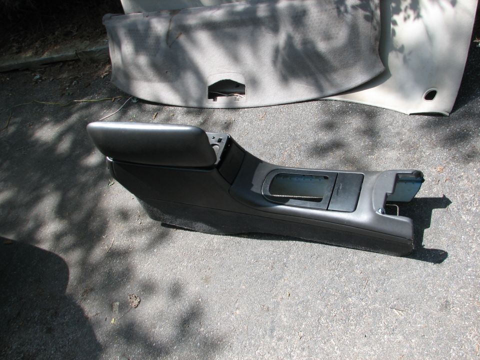 Dark gray car interior center console with armrest and storage compartments, lying on asphalt
