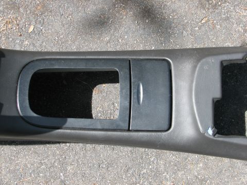 1999 Ford Crown Victoria - A close-up of a car's interior trim piece, likely a center console section, is shown against a gray, pebbled surface.