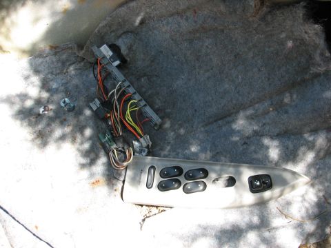 1999 Ford Crown Victoria - A detached car door control panel and its wiring harness lie on a gray carpeted, carpeted surface.