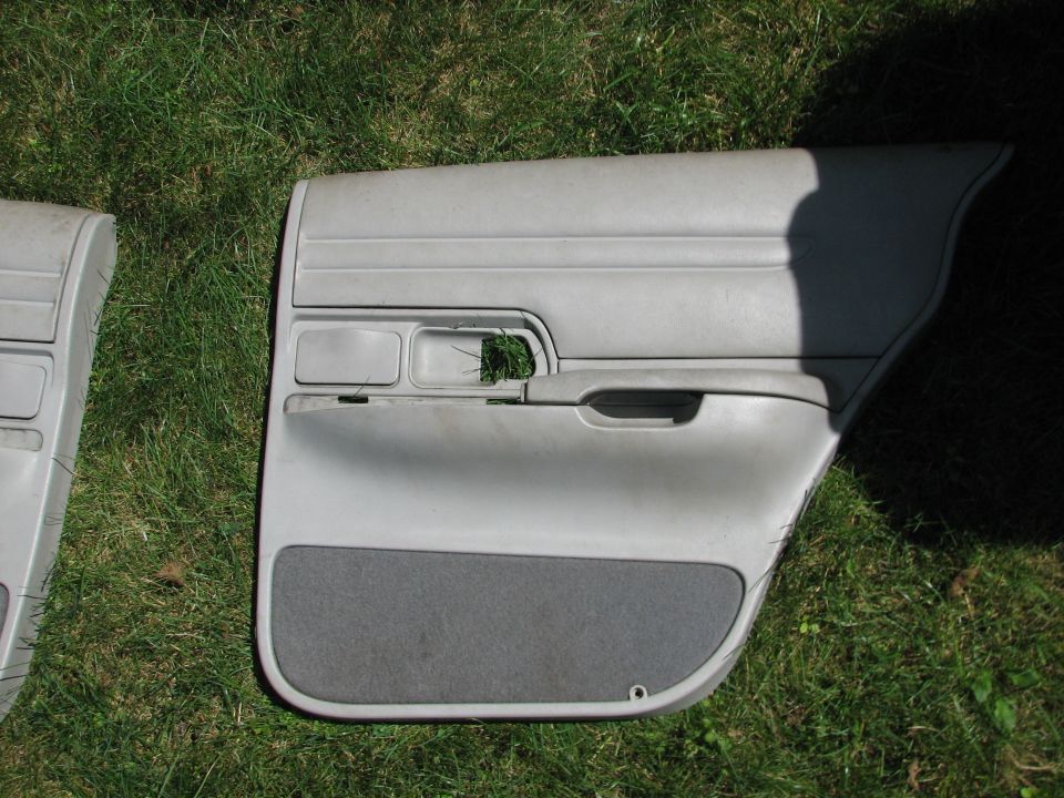 Two gray car door panels lying on grass. One panel has a fabric insert at the bottom