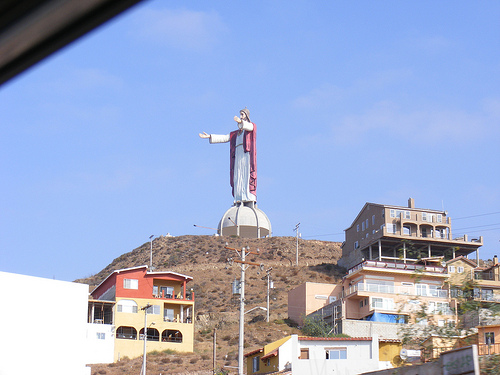 Statue of Jesus Christ on a hill overlooking buildings, with a watermark reading SUPERMOTORS.NET
