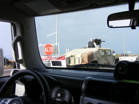 1986 Ford Bronco - A Humvee equipped with a mounted machine gun and a soldier is visible through the windshield, with a stop sign in the background.