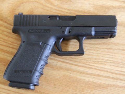 2002 Jeep TJ - A black semi-automatic pistol is shown against a wood grain background.