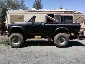 1991 Ford Bronco - A modified black pickup truck with oversized wheels is parked outdoors next to a recreational vehicle.