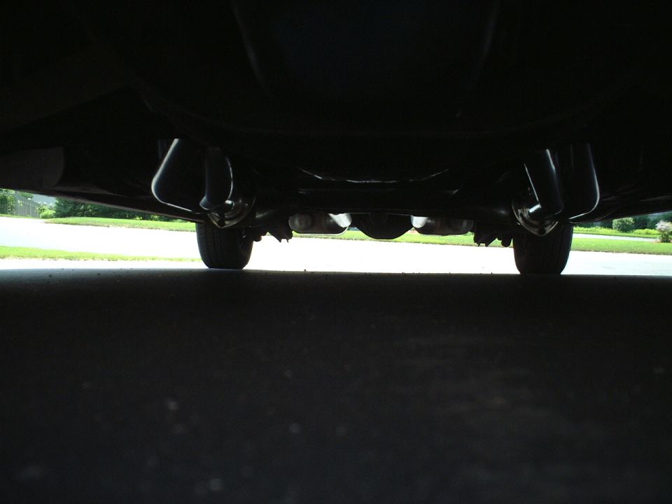 Underside rear view of a vehicle showing axle, exhaust and rear tires from ground level