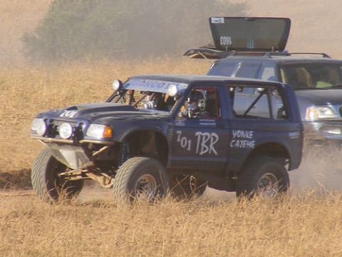 1986 Ford Bronco - A blue off-road race truck, marked with '701 TBR' and 'BRONCO' on its light bar, competes in a dusty race.