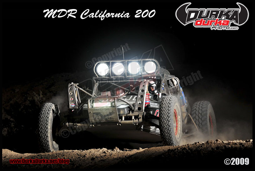 Off-road buggy with four large lights on top, kicking up dust at night