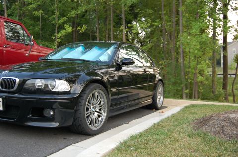 2002 BMW M3 - A black 2002 BMW M3 coupe is parked next to a red truck, with trees in the background.