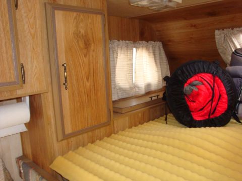 1988 Ford F-350 - The interior of a camper shows wood paneling, a bed, and a window with curtains.