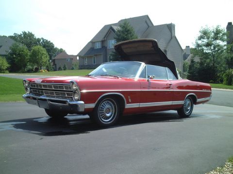 1967 Ford Galaxie - A red 1967 Ford Galaxie convertible is shown with its top partially raised, parked in front of a large house.